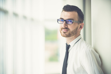 The man in glasses stand near the column in the office