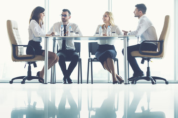 Wall Mural - The four business people sit at the office table near the panoramic window