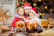 © irena_geo - Three children in hats of Santa Claus sitting with gifts and rejoice