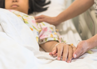 Wall Mural - Nursing caretaker concept with kid patient sleeping in bed with family caregiver hand support in blur medical hospital background (focus on hand)