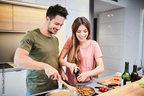 Fotografía Cute joyful couple cooking together and adding spice to meal, laughing and spend