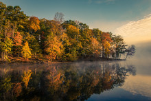Foggy Early Morning Sunrise Over Still Lake With Autumn Trees And Reflections