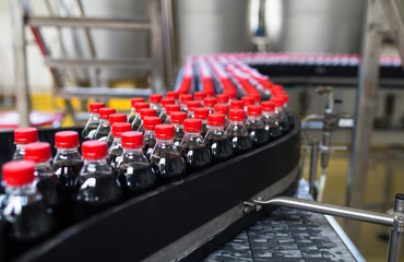 Wall Mural - Bottling factory - Black juice or soft drink bottling line for processing and bottling juice into bottles. Selective focus. 