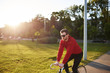 © Anatoliy Karlyuk - Casually dressed young hipster with thick beard enjoying morning bike ride outdoors in urban park with sun shining through trees in background. Serious Caucasian man riding bicycle at weekend