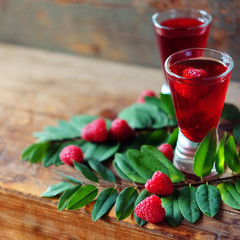 Raspberry fruit liqueur in two shot glasses with berries and green leaves