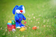 © Alaskajade - Blue easter bunny riding a tricycle with a basket full of colorful easter eggs in the grass.