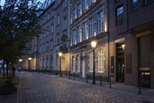 Evening View Of Old, Historical Buildings And Cobblestone Street In Altstadt Dusseldorf. People Walk In Blurry Motion.