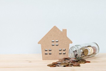 Business, finance, saving money, banking, property loan or mortgage concept :  Wood house model and coins scattered from glass jar on office desk table