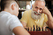 © zinkevych - Cheerful senior man smiling at grandson while playing chess