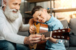 © zinkevych - Smiling grandfather showing grandson how to play guitar