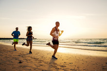 Group Of Sportive People Running On The Beach.