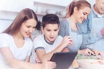 Wall Mural - Charming kids playing on digital tablet while parents cooking