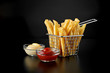 French fries in basket with ketchup and sauce isolated on black background. Front view.