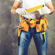 © smspsy - unidentified handyman standing with a tool belt with construction tools and holding roulette against grey background, toned image. DIY tools and manual work concept