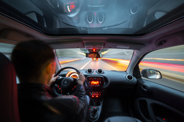 Wall Mural - Urban high spees driving on a smal city car with panoramic roof. View from inside car natural light street and other cars is motion blurred.