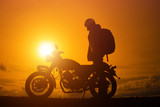 Silhouette of biker man  with his motorbike,he shoulder backpack. beside the natural lake and beautiful, enjoying freedom and active lifestyle, having fun on a bikers tour.sunset background and sky.