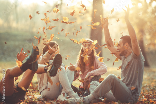 Zdjęcie XXL Grupa przyjaciele relaksuje parka na pięknym jesień dniu. Siedząc na ziemi i rzuca liście w powietrze.