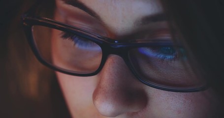 Reflection of a Tablet Computer Screen in Woman Glasses at Night. SLOW MOTION 4K DCi, Dolly Shot. Woman using digital tablet, browsing internet, watching movie. Light reflections in glasses.