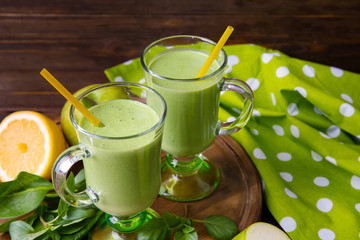 Glasses of green healthy juice with  fruits and herbs on wooden board