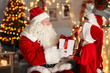 © Africa Studio - Santa Claus giving present to children in room with beautiful Christmas decorations