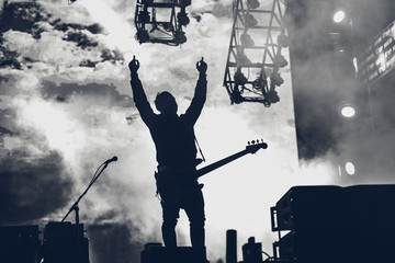 Rock band performs on stage. Guitarist plays solo. silhouette of guitar player in action on stage in front of concert crowd.