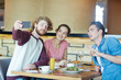 © pressmaster - Cheerful friends sitting in cafe and making selfie by lunch
