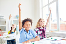 Happy And Clever Learners Of Elementary School Raising Their Hands At Lesson