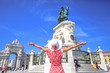 Happy woman with open arms in front of King Dom Jose I equestrian statues in Praca do Comercio or Commerce Square with Triumphal Arch. Female tourist enjoying in Lisbon, Baixa District in a sunny day.