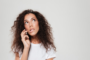 Sticker - Thoughtful curly woman talking by the smartphone and looking up