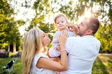 Happy family in a park in summer autumn. Mother, father and baby play in nature in the rays of sunset.