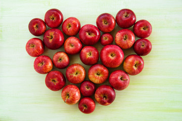 A heart from ripe red apples on the green wooden background, top view.