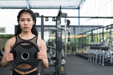 young woman bodybuilder execute exercise in fitness center. female athlete lift heavy weight barbell plate in gym. sporty girl working out in health club.