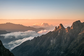 Poster -  mountain tops of the cliffs illuminated by the setting light of the sun and clouds down in the valley