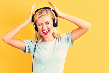 Wall Mural - Happy young woman with headphones on a yellow background