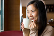 © toonzzz - Asian woman drinking coffee from white coffee cup with blurry background of coffee shop