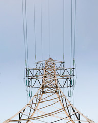 Lonely metal mast power lines with wires standing vertically from below against a blue sky day.