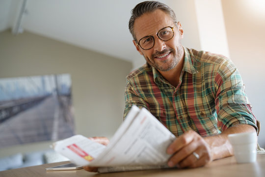 Handsome mature man at home reading newspaper