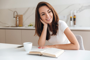 Wall Mural - Smiling girl reading a book while sitting at the table