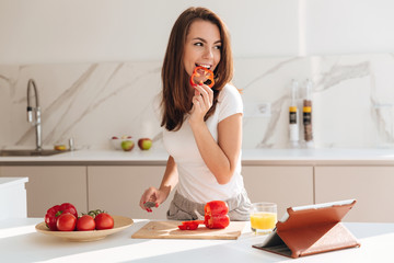 Wall Mural - Young smiling woman eating vegetables while making a salad