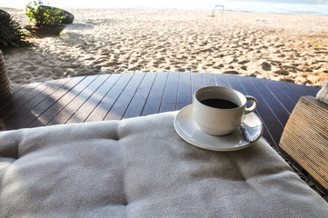 Close up coffee cup on wood table, coffee cup on the beach background, white cup of hot coffee on beach