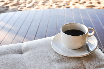 Wall Mural - Close up coffee cup on wood table, coffee cup on the beach background, white cup of hot coffee on beach