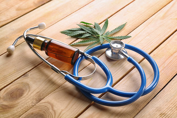 Wall Mural - Stethoscope with hemp leaves and bottle of oil on wooden background. Alternative medicine concept