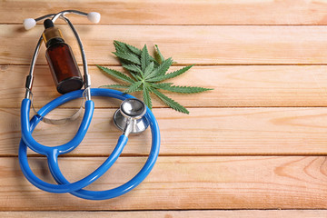 Wall Mural - Stethoscope with hemp leaves and bottle of oil on wooden background. Alternative medicine concept