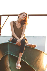 Wall Mural - Fashionable young woman sitting on boat at river port