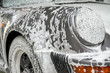 Retro silver sports car in a car wash. The car is covered in white cleaning foam and is about to be sprayed with water.