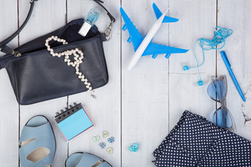 blue bag, sunglasses, sandals, nail polish, earphone note pad and little airplane on white wooden background