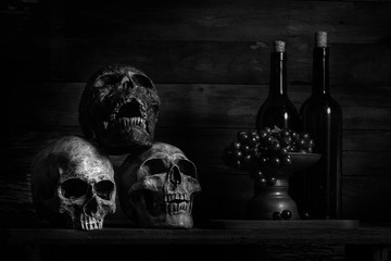 Wall Mural - still life photography, human skulls, book, wine and grap on black table against art dark background  with window light