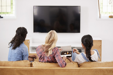 Wall Mural - Female Friends Sitting On Sofa Watching Television Eating Candy