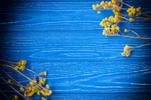 Dry Yellow Flowers Forming A Frame On A Bright Blue Wooden Background With Dark Edges (with Copy Space In The Center For Your Text)
