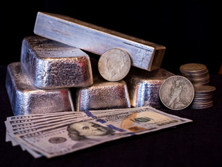 Several Silver Bars with Two Silver Dollars , a stack of Silver Half Dollars and Paper money.